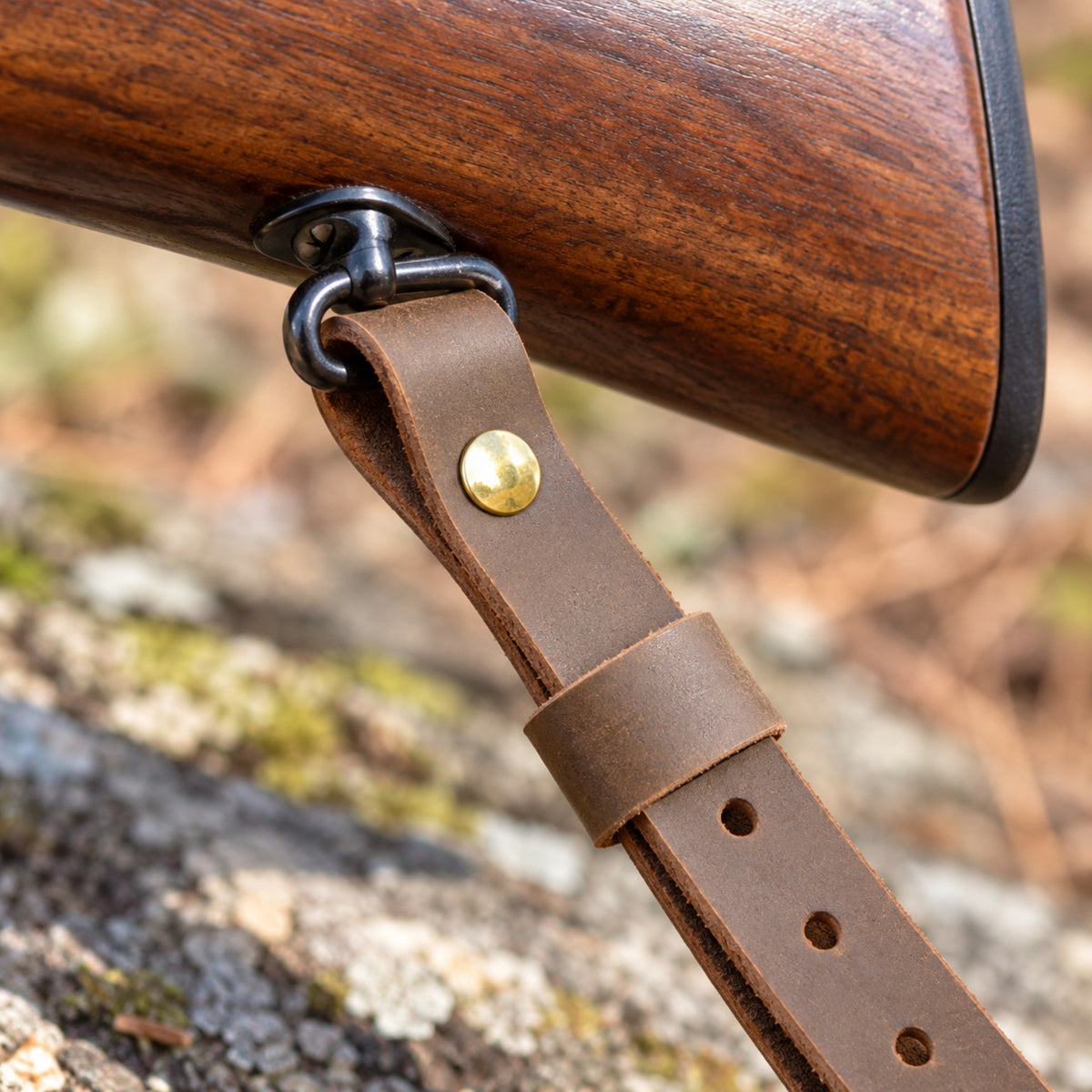 One-inch brown leather rifle sling attached to the swivel of a wooden rifle stock