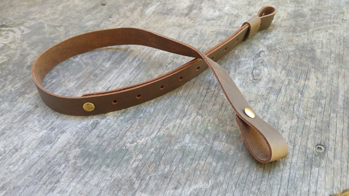 Handcrafted adjustable brown leather rifle sling laid flat on weathered wood